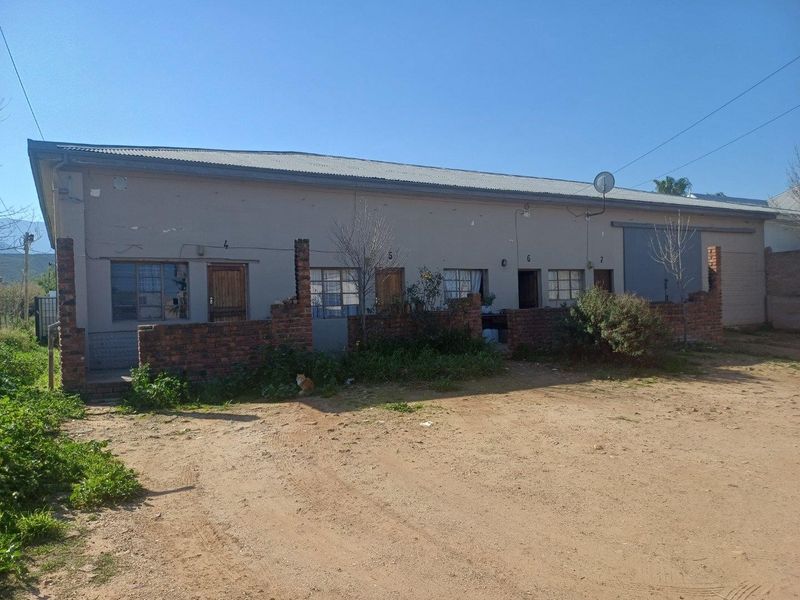 Front elevation of a commercial building featuring multiple unit entrances, industrial sliding door, and a corrugated metal roof with a surrounding brick boundary wall.