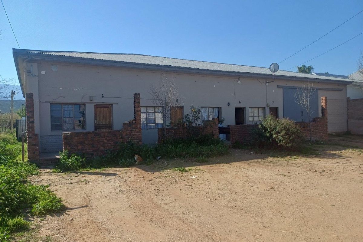Front elevation of a commercial building featuring multiple unit entrances, industrial sliding door, and a corrugated metal roof with a surrounding brick boundary wall.