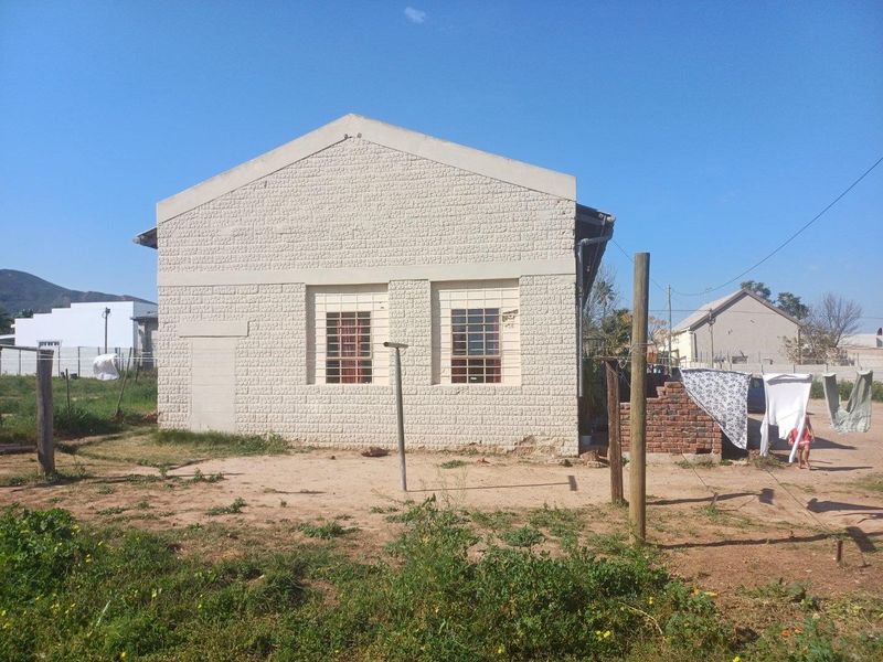 Rear view of a commercial building featuring a textured brick facade, security-barred windows, and a gable roof structure set on a dirt lot.