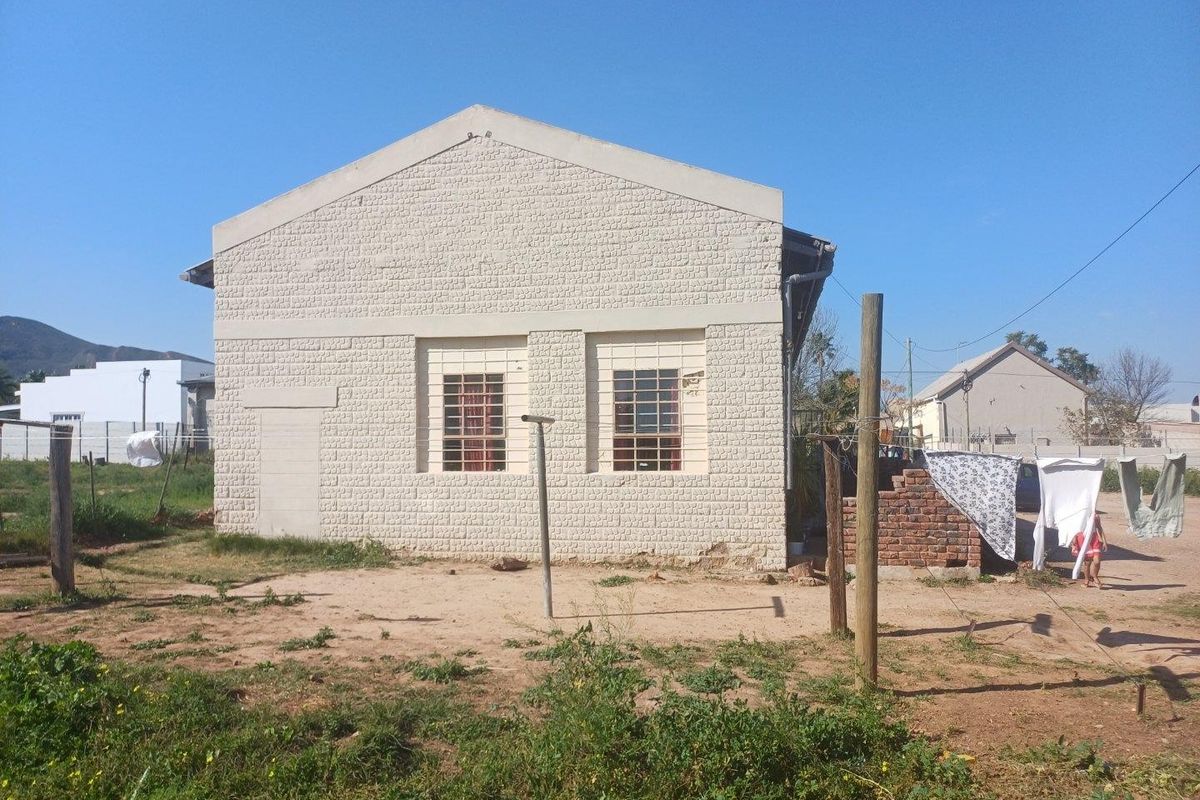 Rear view of a commercial building featuring a textured brick facade, security-barred windows, and a gable roof structure set on a dirt lot.