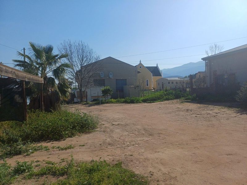 An exterior view of the rear yard area featuring unpaved ground, perimeter fencing, and views of adjacent commercial or residential structures.