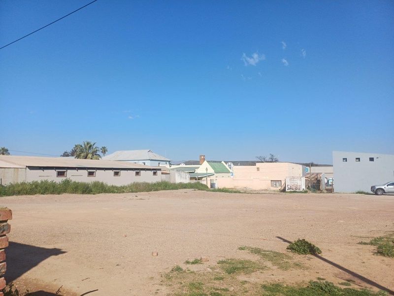 An expansive, unpaved commercial lot featuring surrounding boundary walls and views of adjacent building structures.