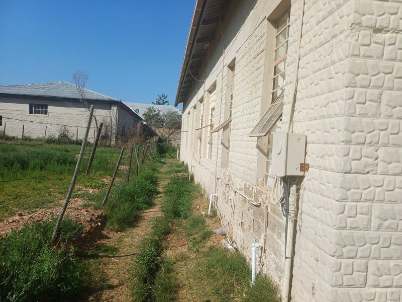 Side view of the commercial building showing textured masonry walls, metal-framed windows, and external utility connections along a grassed perimeter area.