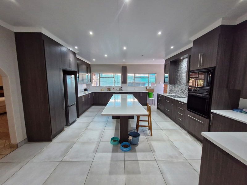 Spacious modern kitchen featuring dark wood cabinetry, a large central island with stone countertops, built-in oven, and neutral tiled flooring.