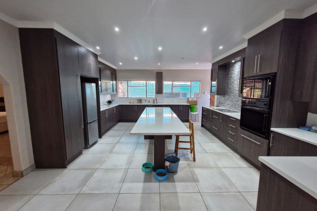 Spacious modern kitchen featuring dark wood cabinetry, a large central island with stone countertops, built-in oven, and neutral tiled flooring.