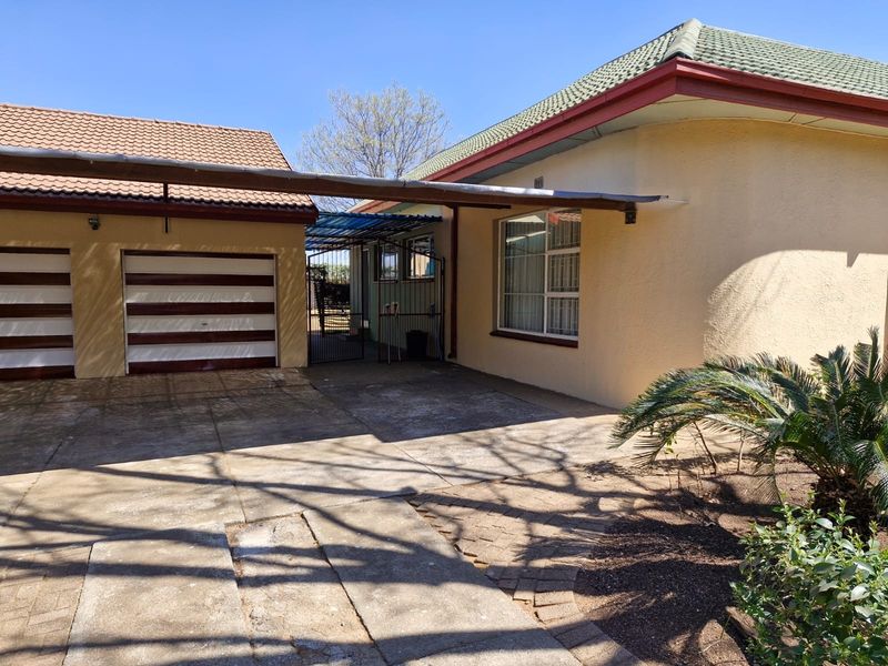 Front exterior view showing a double garage, paved driveway, and covered carport area with established garden features.