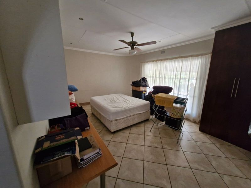 A bedroom featuring tiled flooring, built-in cupboards, and a ceiling fan, offering a functional space ready for personalization.