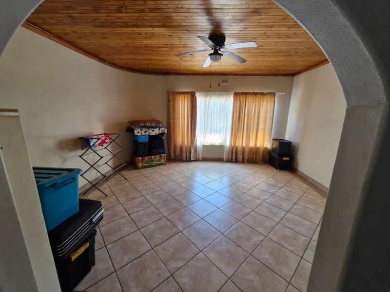 A spacious living area featuring a timber-clad ceiling, ceiling fan, and neutral tiled flooring, accessed through a classic arched doorway.
