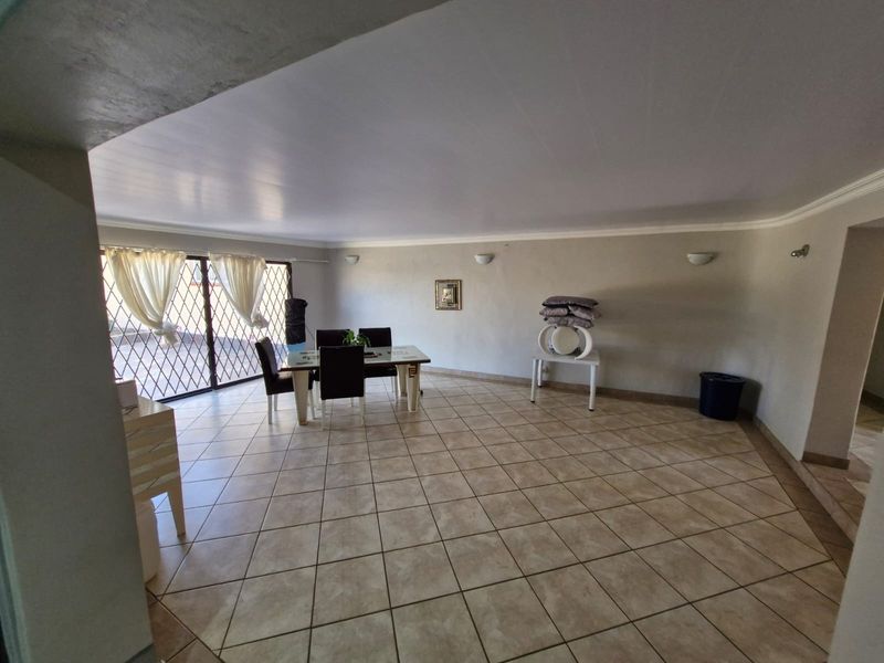 Spacious living area featuring neutral ceramic floor tiles, wall-mounted lighting, and a large sliding glass door with security gate access.