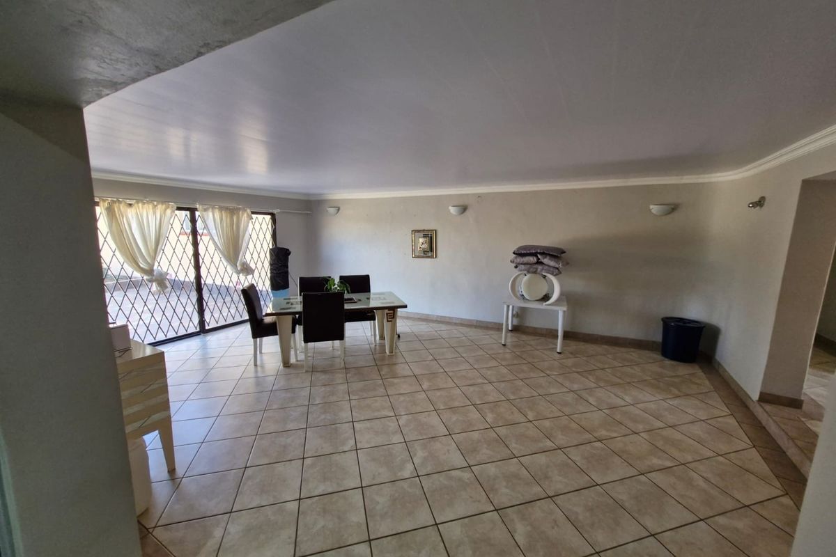 Spacious living area featuring neutral ceramic floor tiles, wall-mounted lighting, and a large sliding glass door with security gate access.