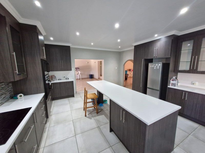 Modern kitchen featuring dark wood cabinetry, white stone countertops, a central island, and tiled flooring with recessed ceiling lighting.