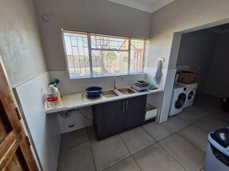 Functional laundry area featuring tiled flooring, a stainless steel double sink with mixer tap, built-in cabinetry, and dedicated space for laundry appliances.