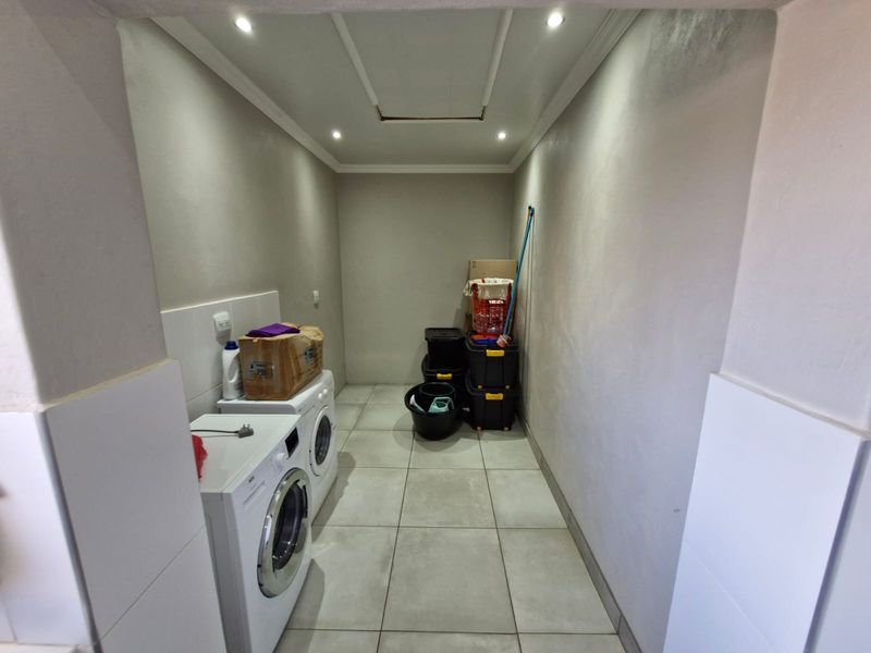 A functional laundry area featuring tiled flooring, recessed lighting, and a tiled splashback, providing a practical space for washing and utility tasks.
