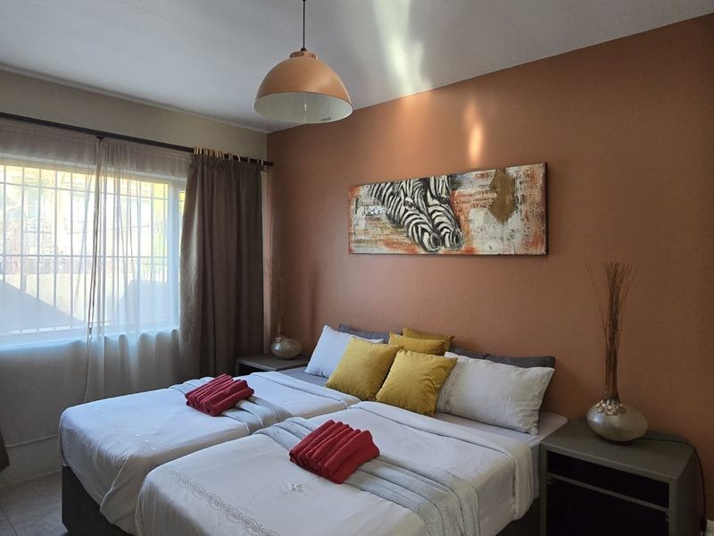 A cozy bedroom featuring a built-in wardrobe, a pendant light fixture, and a window fitted with security bars.