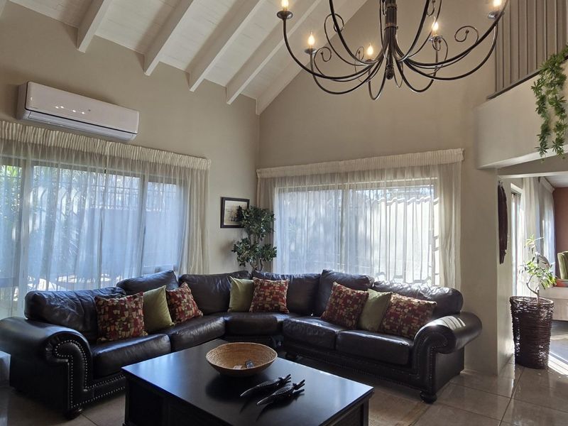 Spacious living room featuring a high vaulted ceiling with exposed rafters, tiled flooring, and a split-system air conditioner, overlooking a mezzanine level.