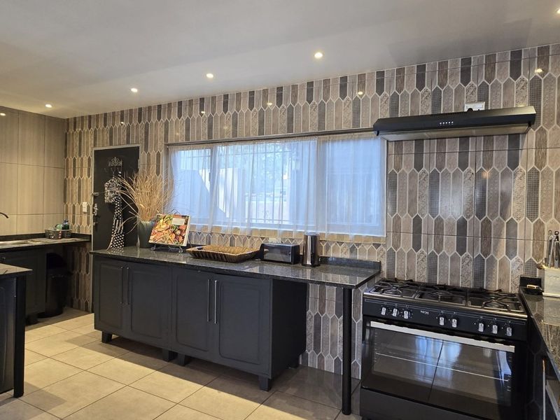 Modern kitchen featuring dark cabinetry, granite countertops, a gas stove with extractor fan, and a decorative tiled backsplash.