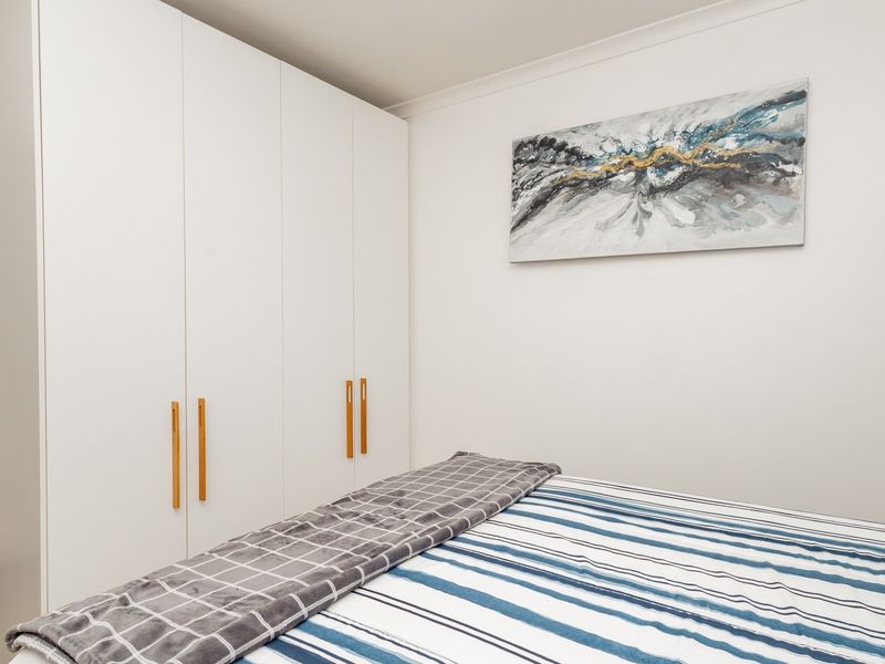 A clean and well-maintained bedroom featuring a large, modern white built-in wardrobe with minimalist wooden handles.