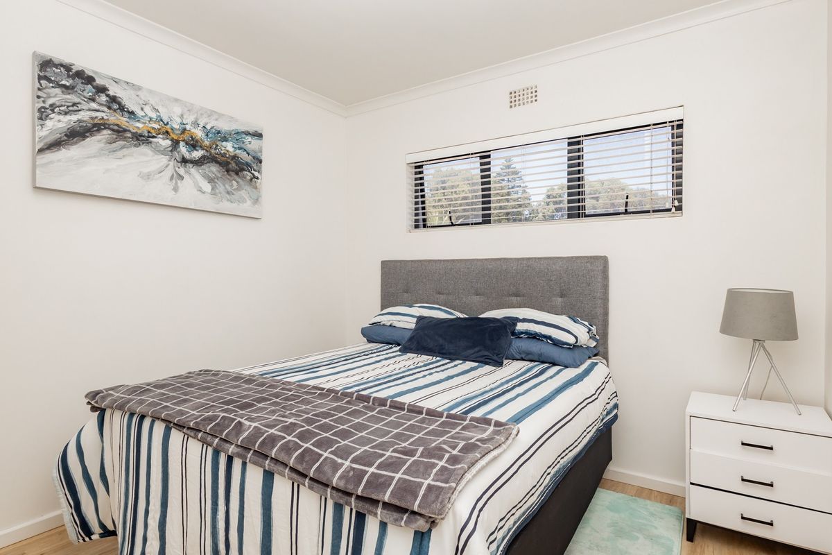 A well-maintained bedroom featuring neutral walls, laminate flooring, and a window fitted with venetian blinds and a ventilation grille.