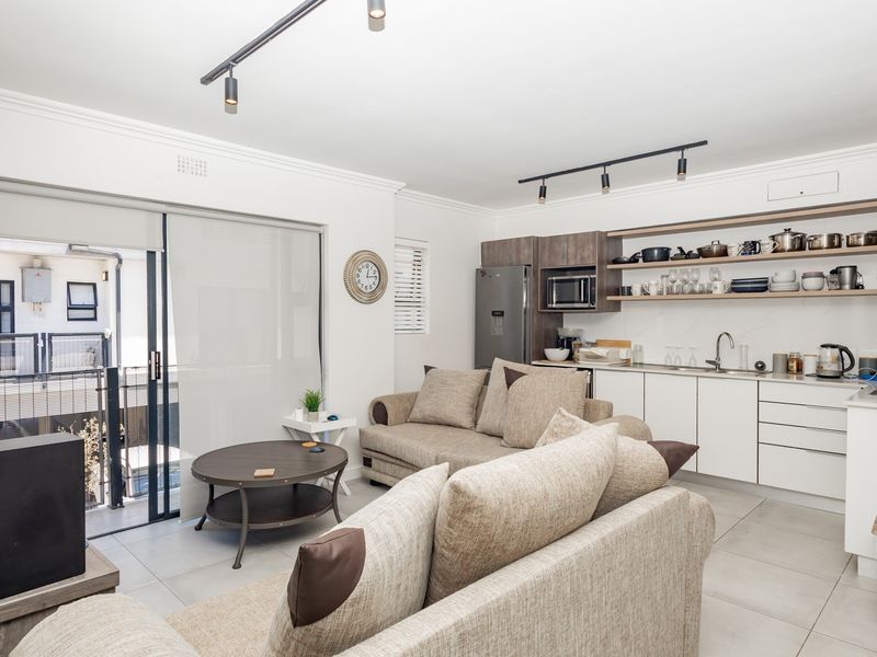 Modern open-plan living area featuring a sleek kitchen with built-in cabinetry, open shelving, and direct access to a private balcony through sliding doors.