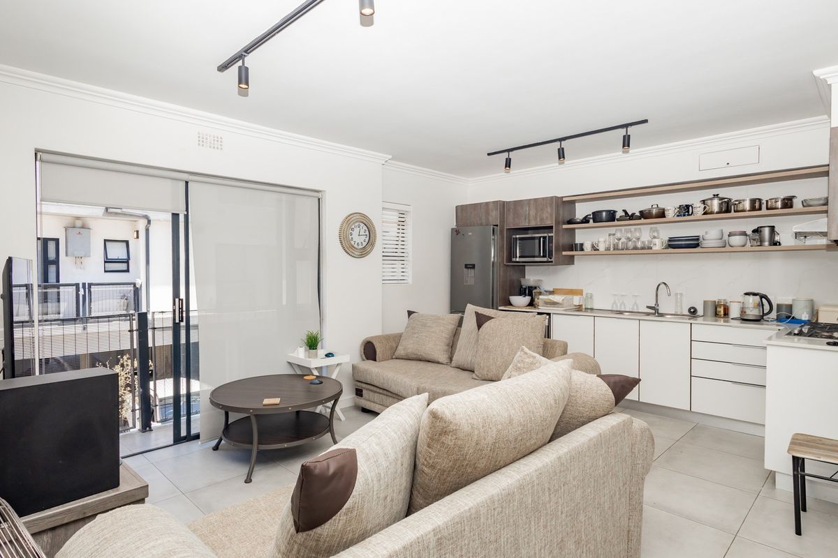 Modern open-plan living area featuring a sleek kitchen with built-in cabinetry, open shelving, and direct access to a private balcony through sliding doors.