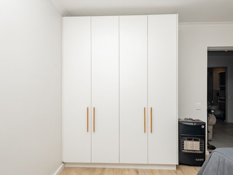 A bedroom featuring a modern, full-height white built-in wardrobe with sleek handles and light-toned laminate flooring.