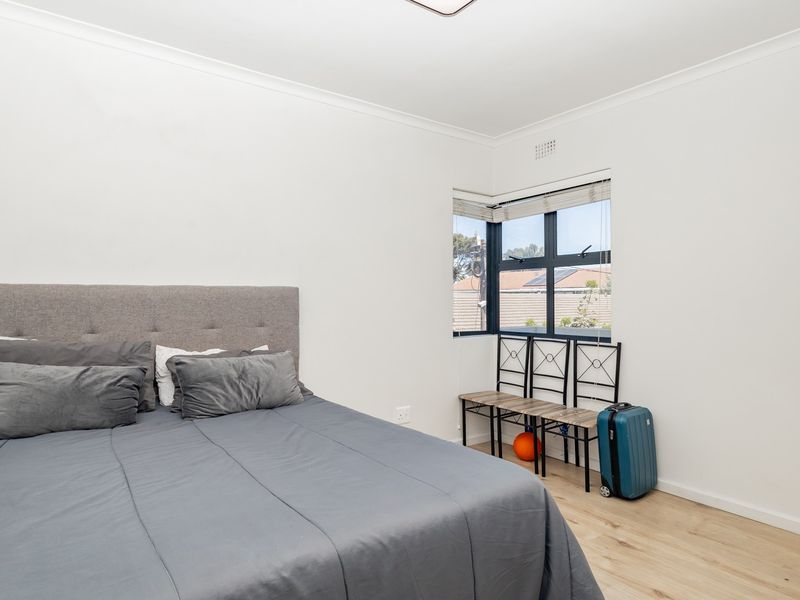 A bright bedroom featuring light-toned laminate flooring, neutral walls, and a corner window that allows for natural light.