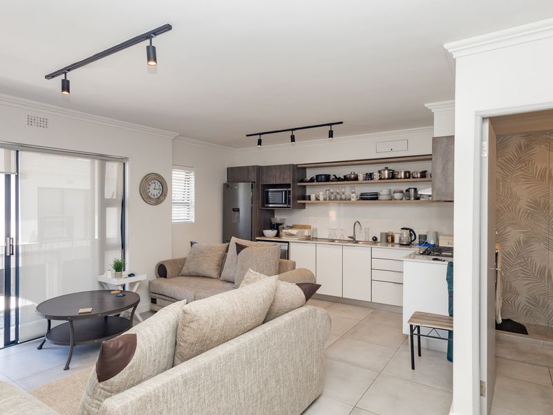 Modern open-plan living area featuring a sleek kitchen with built-in appliances, tiled floors, and direct access to a balcony, adjacent to a contemporary bathroom.