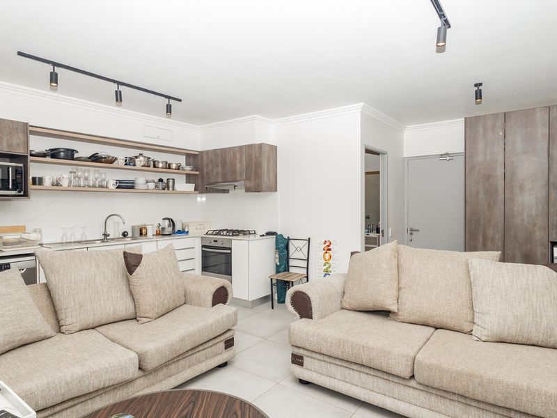 Modern open-plan living area featuring a well-equipped kitchen with built-in cabinetry, gas hob, and integrated laundry facilities, finished with neutral tiled flooring.