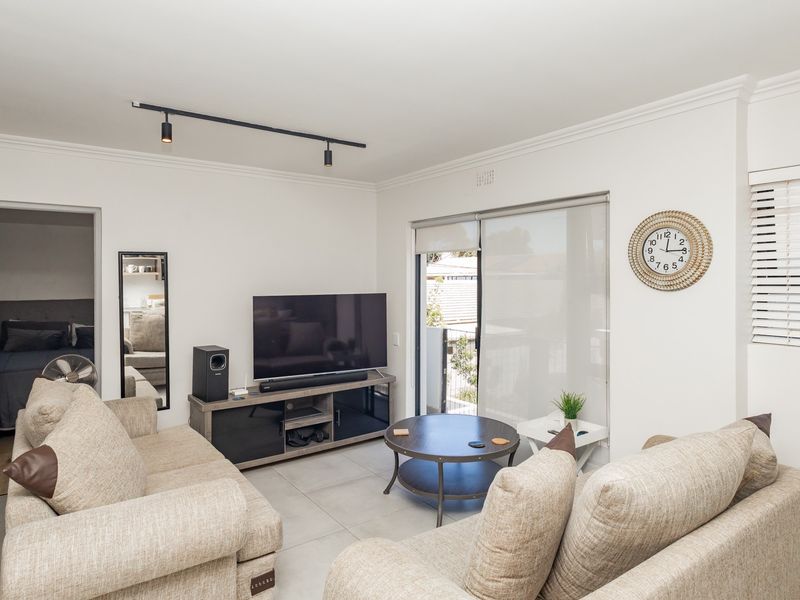 A bright living room featuring tiled flooring, track lighting, and a sliding glass door providing access to the outdoor area.