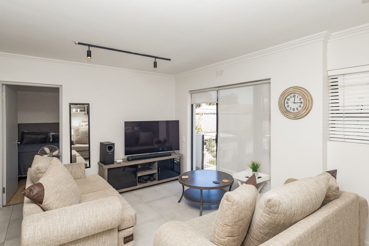 A bright living room featuring tiled flooring, track lighting, and a sliding glass door providing access to the outdoor area.