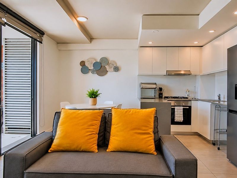 Modern open-plan apartment featuring a compact kitchen with built-in appliances, flowing into a living area with direct access to a private balcony.