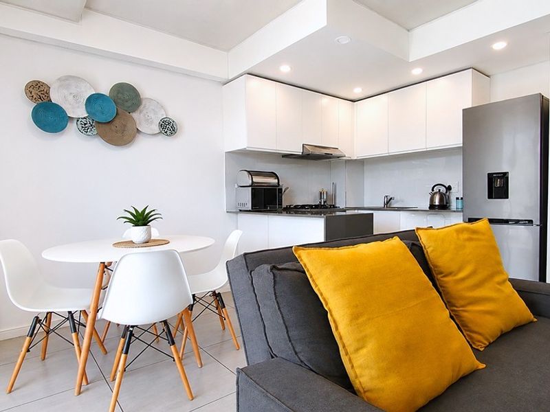 Modern open-plan living area featuring a compact kitchen with white cabinetry, gas hob, and tiled flooring, seamlessly integrated with the dining and lounge space.
