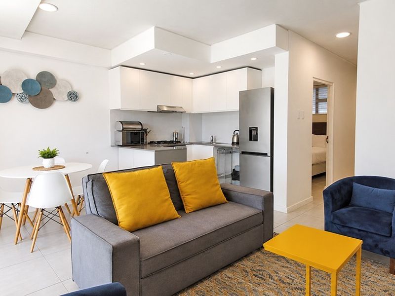 Modern open-plan living area featuring a compact kitchen with white cabinetry and tiled flooring, seamlessly flowing into the lounge space.