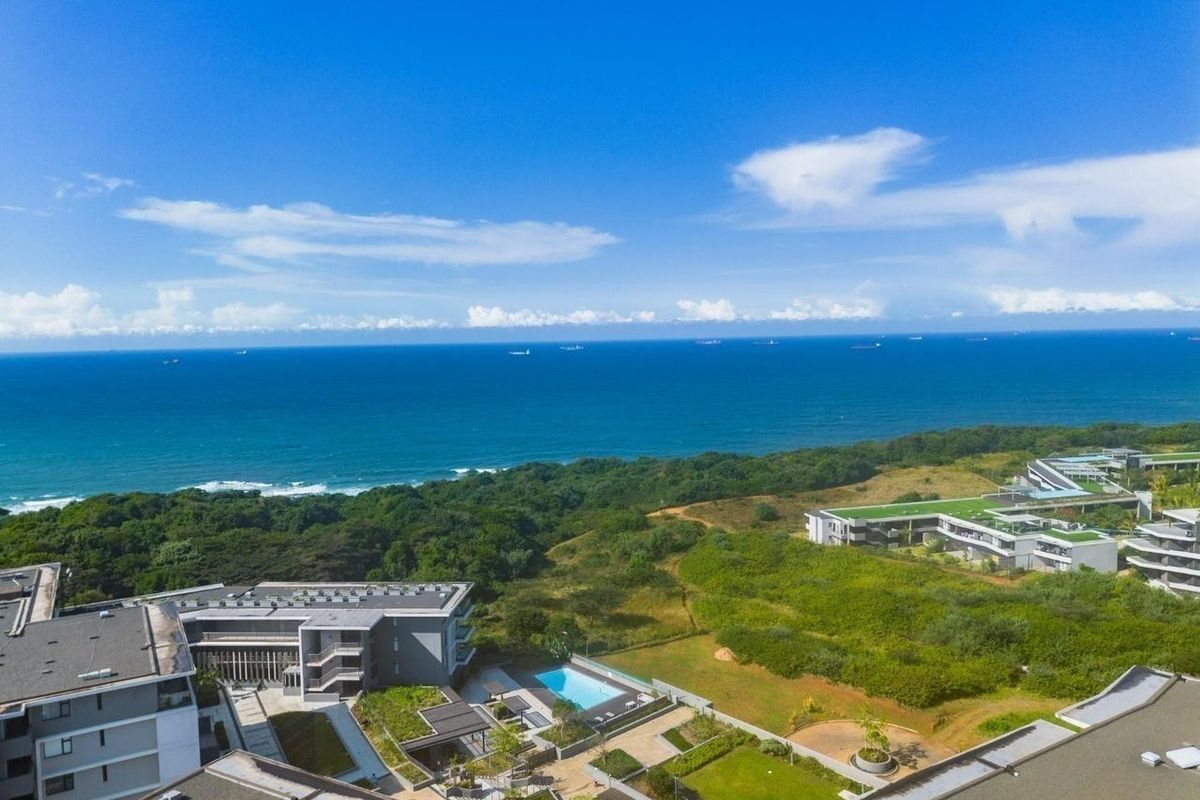 Aerial view of the apartment complex featuring a swimming pool, landscaped grounds, and proximity to the coastline and ocean.