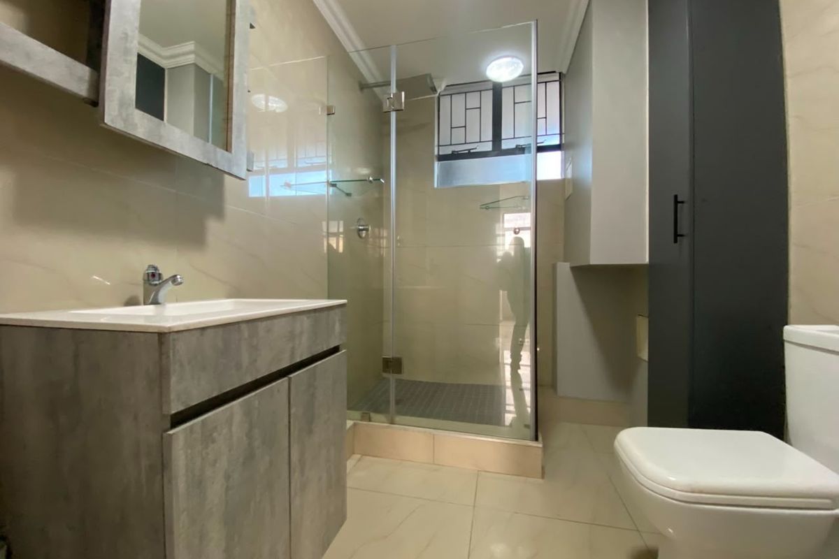 Modern bathroom featuring a glass-enclosed shower, vanity cabinet with basin, and neutral wall and floor tiling.