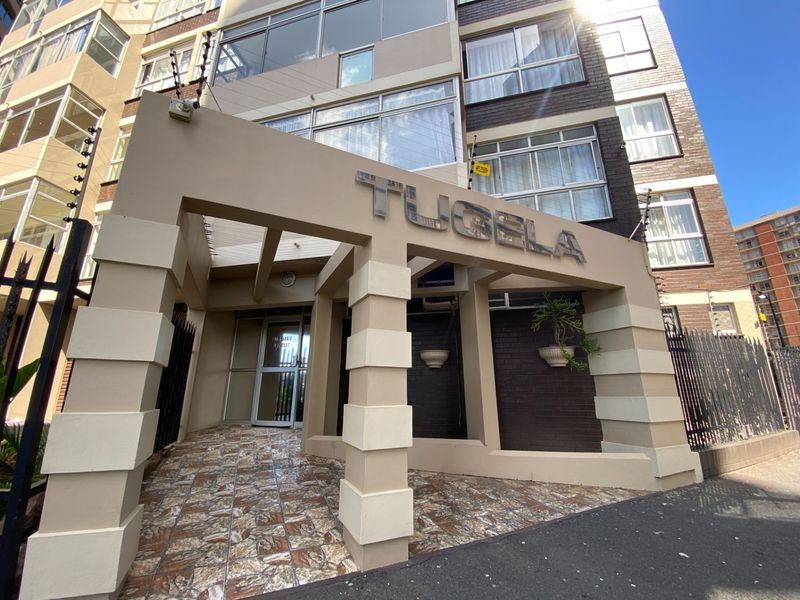 The front entrance of the Tugela apartment building, featuring a covered walkway, brick facade, and secure perimeter fencing.