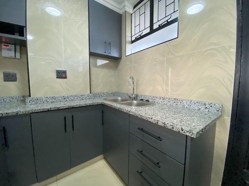 A modern, well-maintained kitchen featuring dark grey cabinetry, granite countertops, a double bowl sink, and neutral tiled walls.