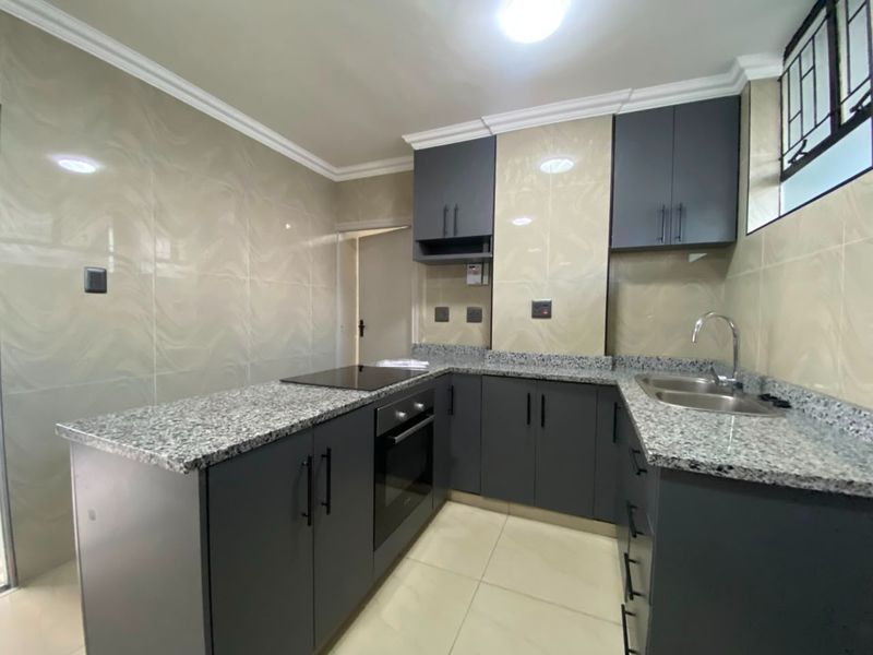 Modern kitchen featuring dark grey cabinetry, granite countertops, built-in oven, electric hob, and neutral tiled splashbacks in a clean, well-maintained space.