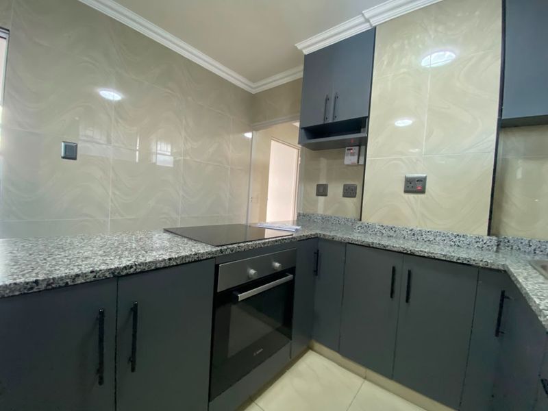 Modern kitchen featuring dark grey cabinetry, granite countertops, built-in oven, and electric hob with a stylish tiled backsplash.