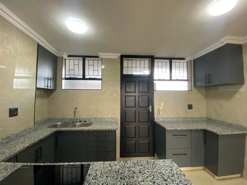 A modern, well-maintained kitchen featuring dark cabinetry, granite countertops, a double basin sink, and tiled backsplash with secure window fittings.