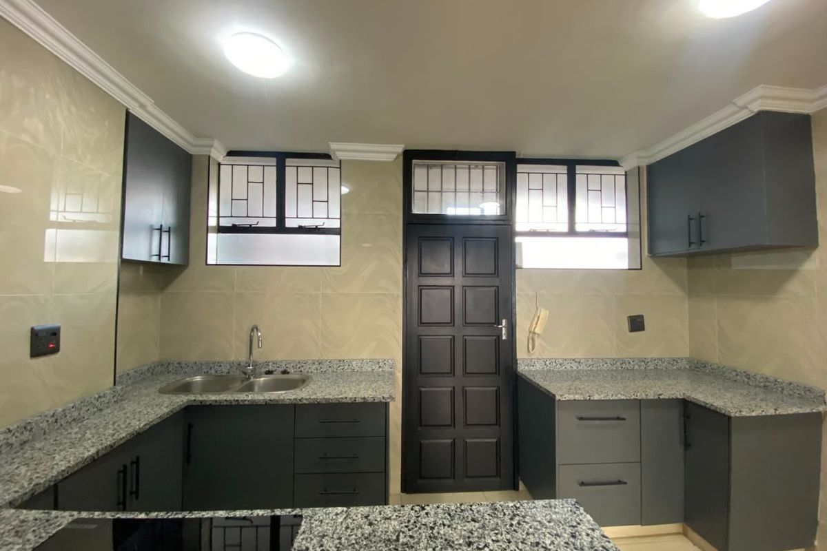 A modern, well-maintained kitchen featuring dark cabinetry, granite countertops, a double basin sink, and tiled backsplash with secure window fittings.