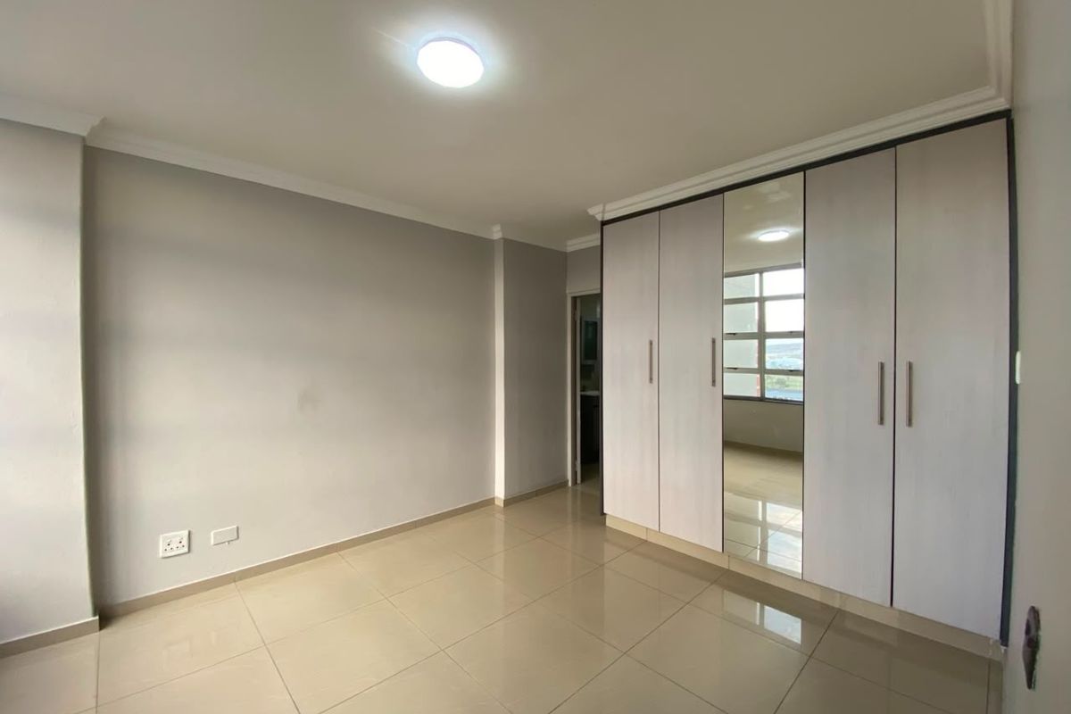 A bright, empty bedroom featuring neutral tiled flooring, cove cornicing, and a large built-in wardrobe with a central mirrored panel.
