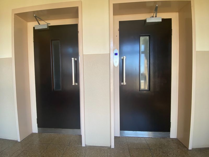 A clean and functional apartment hallway featuring two elevator doors with stainless steel handles and overhead door closers.