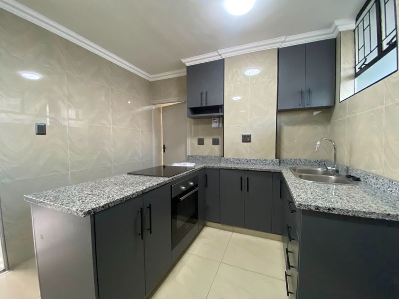 Modern kitchen featuring dark grey cabinetry, granite countertops, built-in oven, electric hob, and double sink with tiled splashback.
