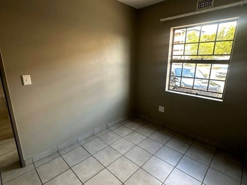 An empty bedroom featuring neutral wall paint, tiled flooring, and a window fitted with security bars.