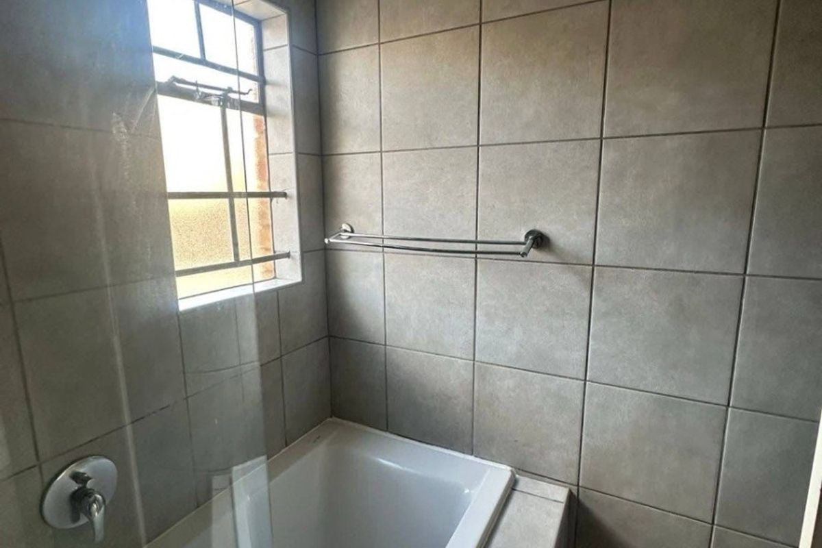 A clean bathroom featuring a built-in bathtub with a glass screen, neutral wall tiling, and a functional towel rail.