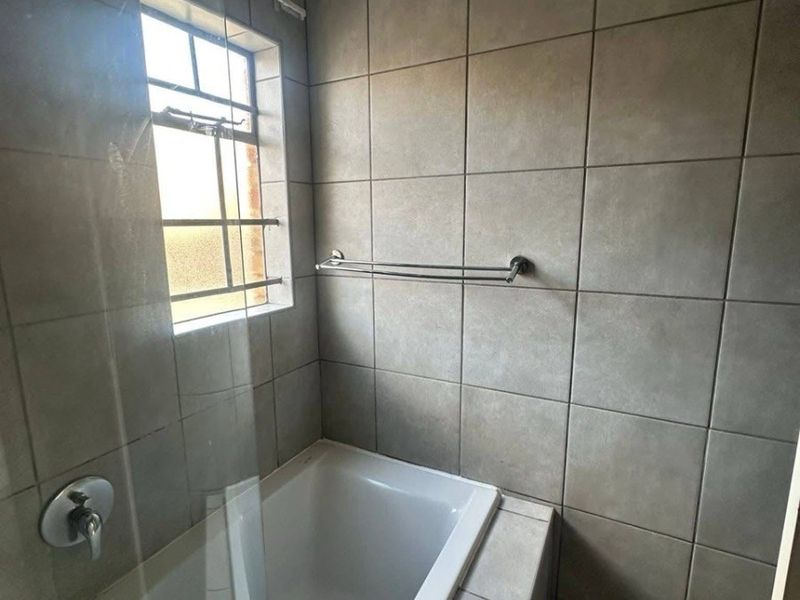 A clean bathroom featuring a built-in bathtub with a glass screen, neutral wall tiling, and a functional towel rail.
