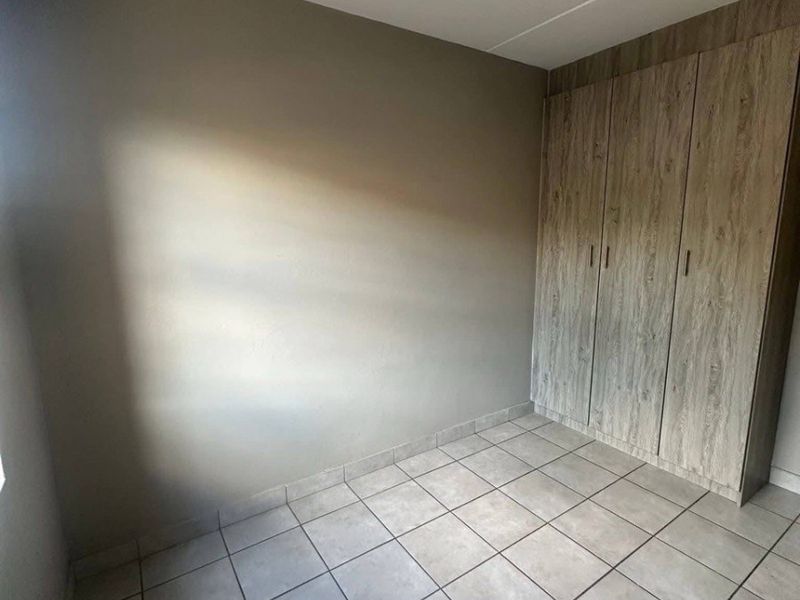 A clean, empty bedroom featuring neutral wall paint, light-toned built-in cupboards, and practical tiled flooring.