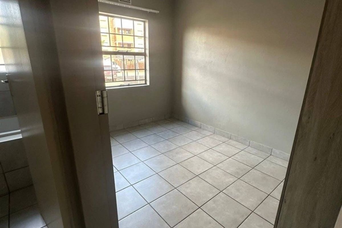 An empty bedroom featuring neutral wall paint, tiled flooring, and a window with security bars.