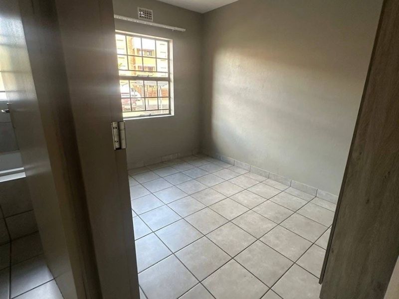 An empty bedroom featuring neutral wall paint, tiled flooring, and a window with security bars.